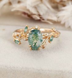 an oval shaped green ring with leaves and stones on the side, sitting on a white surface