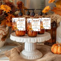 three bottles of soap sitting on top of a cake plate with pumpkins in the background