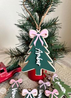 christmas tree shaped cookies are sitting next to a red truck and pine tree with pink bows