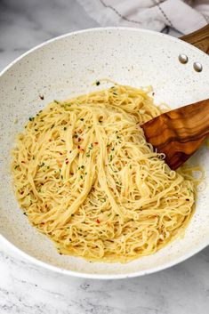 a white bowl filled with pasta and a wooden spatula on a marble counter top