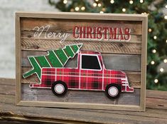 a red truck with a christmas tree on the back sits in front of a wooden sign