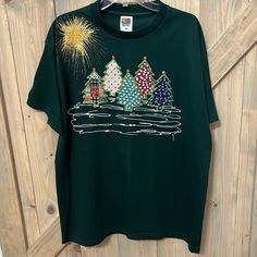 a green t - shirt with christmas trees and fireworks on the front is hanging on a wooden wall