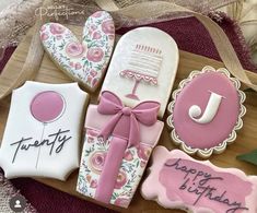 decorated cookies with pink and white icing are on a wooden tray next to a ribbon