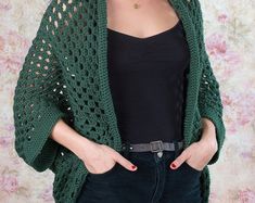 a woman wearing a green crocheted cardigan and black top with her hands in her pockets