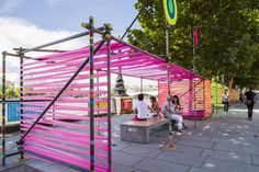 people are sitting on benches in front of colorfully painted structures and trees near the water