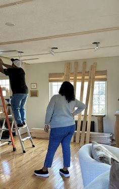 two people standing on ladders in a living room