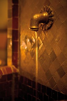 a gold faucet with water running from it's sides in a bathroom