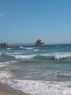 the ocean with waves crashing on it and a pier in the distance