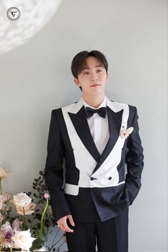 a man in a tuxedo standing next to flowers