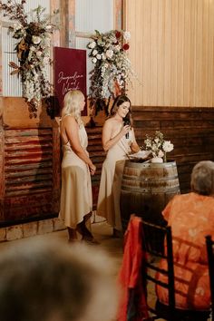 two women standing next to each other in front of a barrel with flowers on it