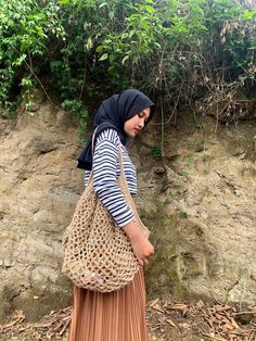 a woman in hijab carrying a bag on her back while standing next to a stone wall