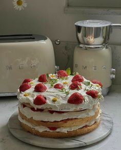 a cake with white frosting and strawberries sitting on a counter next to a toaster