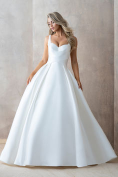 a woman in a white wedding dress standing against a wall with her hands on her hips