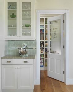 a kitchen with white cabinets and wooden floors, an open door leading to the pantry