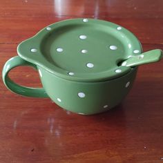 a green bowl with white polka dots sits on a wooden table next to a spoon