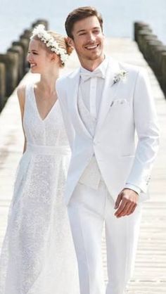 a man and woman dressed in white walking down a pier