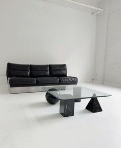 a black leather couch sitting next to a glass table on top of a white floor