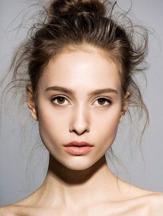 a woman with her hair in a messy topknot looks at the camera while wearing makeup