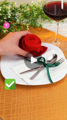 a person holding a rose on a plate next to a glass of wine and spoons