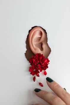 a woman's hand with green fingernails holding a red flower in front of her ear