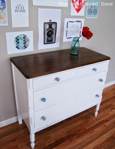 a white dresser with drawers and pictures on the wall