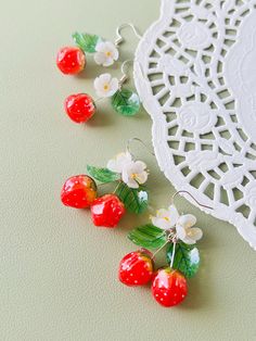 four red cherries with green leaves and white flowers are on a doily next to a lace doily