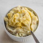 a white bowl filled with mashed potatoes on top of a table next to a spoon