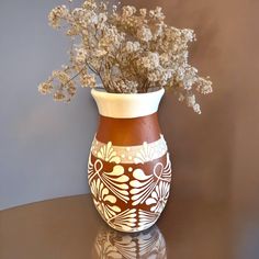 a brown and white vase sitting on top of a table filled with lots of flowers