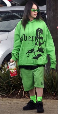 a woman in green sweatshirt and shorts walking down the street