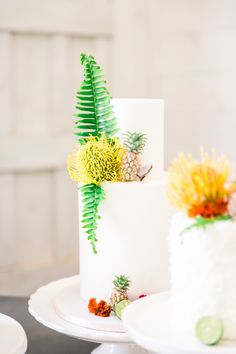 two tiered white wedding cake decorated with tropical flowers and greenery on each layer