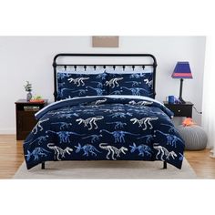 a bed with blue and white dinosaur comforter set on it in a bedroom setting