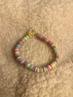 a bracelet that is laying on top of a white blanket with a gold beaded charm