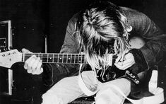 a man with long hair playing an electric guitar in a black and white photo, while sitting on a chair