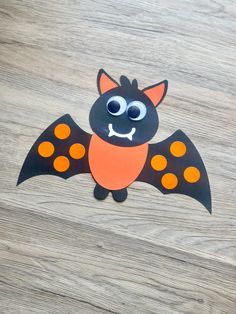 a paper cut out of a bat on a wooden surface with eyes and nose painted orange