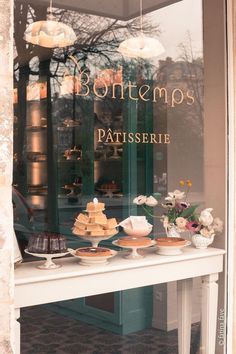 there is a table with cakes on it in front of the storefront window that says bontemps patisserie