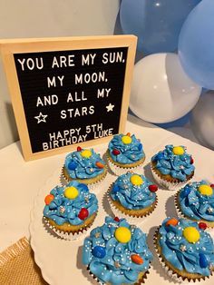 cupcakes with blue frosting are on a plate next to a sign that says you are my sun, my moon and all my stars