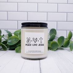 a candle with the words pray on it sitting next to some green leaves and a white brick wall