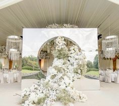 an outdoor wedding setup with white flowers and chandelier hanging from the ceiling, in front of a large mirror