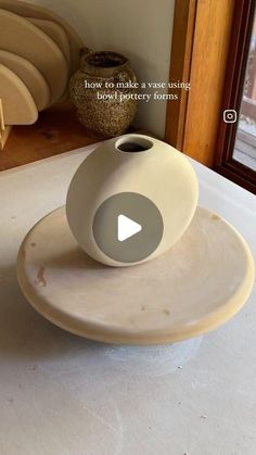 a white vase sitting on top of a table next to a window with the words how to make a vase using bake pottery forms