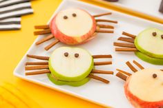 two apples with faces made out of cinnamon sticks and apple slices on a white plate