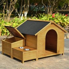 a wooden dog house with its door open and two bowls in the bottom compartment on the ground