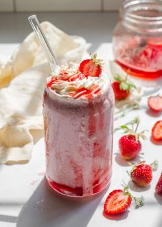 a strawberry milkshake with whipped cream and strawberries next to it on a table