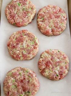 four hamburger patties sitting on top of a white paper lined baking sheet with green sprinkles