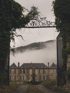 an iron gate leading to a large building with ivy growing on it's sides