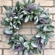 a wreath with purple flowers and green leaves on a brick wall