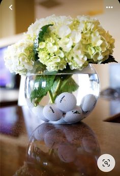 a vase filled with white flowers and golf balls on top of a wooden table next to a tv