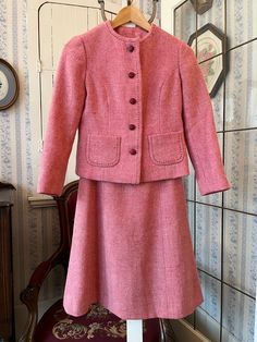 This gorgeous suit is made from a wool blend in a lovely shade of rose pink, with decorative dark red stitching around the collar, front edge and pockets. The jacket has the original red buttons in the front and two front pockets, and is fully lined with light pink silky lining. The measurements, taken with the jacket lying flat, are: shoulder to shoulder, 14 inches; armpit to armpit, 17 inches; sleeves, 21 inches; length, 19 inches; bottom edge, 20 inches. The matching A line skirt has a zipper and metal clasp in the back and is also fully lined The measurements, taken with the skirt lying flat, are: waist, 12 1/2 inches; hips, 20 inches; length, 22 inches; bottom edge, 26 inches. Both pieces are in very good condition. Fitted Pink Wool Outerwear, Pink Fitted Wool Outerwear, Tailored Pink Wool Outerwear, Tailored Pink Suit For Fall, Tailored Pink Suits For Fall, Fitted Pink Winter Suits, Pink Winter Suits For Formal Occasions, Fitted Pink Skirt Suit For Winter, Elegant Pink Skirt Suit For Fall