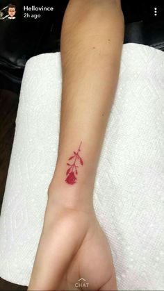 a small tattoo on the wrist of a person's hand with a red flower