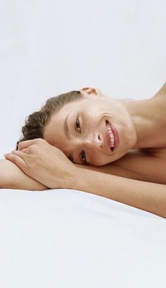 a woman laying on top of a bed next to a white wall with her arms crossed