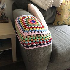 a crocheted pillow sitting on top of a gray couch next to a table